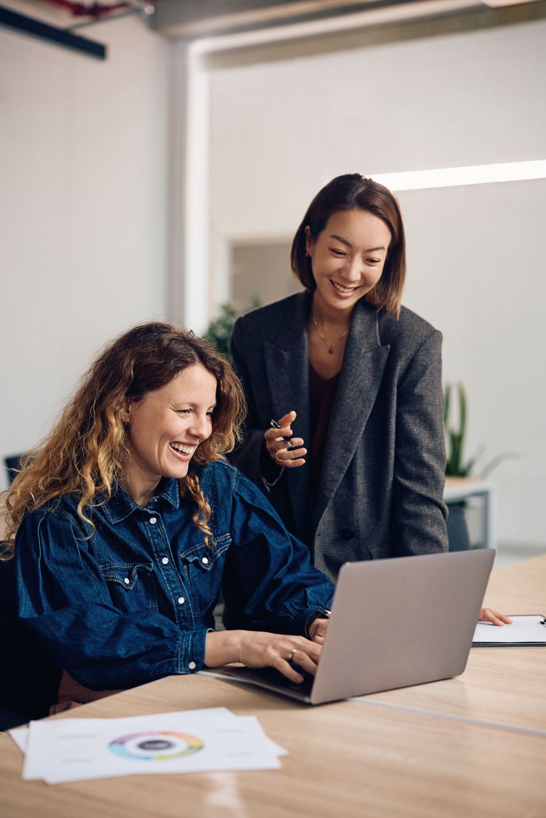 Zwei Frauen arbeiten gemeinsam lachend an einem Laptop